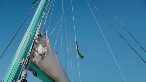 A-shot-from-below-os-a-mast-with-many-straight-strings-going-up,-and-part-of-the-boom-with-the-sail-stayed