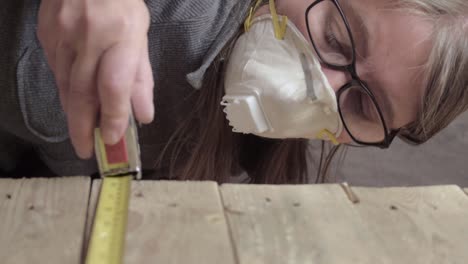 Woman-wearing-disposable-dust-mask-while-measuring-wood