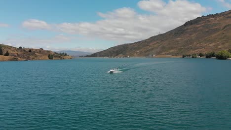 Waterskiing-behind-boat-on-Lake-Dunstan-near-Clyde-dam,-Central-Otago,-New-Zealand-with-mountains-and-clouds-in-background