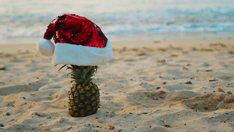 Strand-In-Curaçao-–-Ananas-Mit-Roter-Weihnachtsmütze-Am-Sandstrand-Mit-Meereswellen-Im-Hintergrund-–-Nahaufnahme