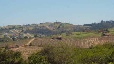 Distant-view-of-simple-small-farms-on-the-hills-of-Brazil,-divided-by-dirt-roads-and-paths-leading-to-small-farmer-houses-in-the-middle-of-the-crops-in-a-calm-spring-morning