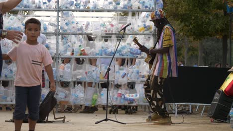 Guitar-musician-with-dreadlocks-playing-near-a-wall-of-recycled-plastic-bottles-during-the-annual-festival-of-La-Merce