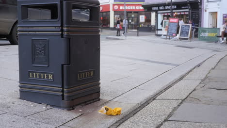 Litter-not-properly-thrown-in-public-trash-bin-and-people-ignore-walking-pass,-medium-shot