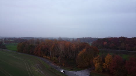Landing-drone-shot-showing-person-alone-with-car-in-autumn-forest,-wide-shot