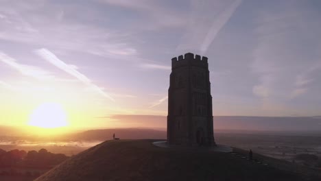 Zooming-out-aerial-shot-of-the-sunrise-over-Glastonbury-Tor,-Somerset