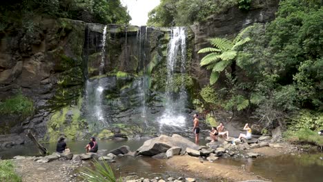 Slowmo---Gruppe-Junger-Leute-Sitzt-An-Den-Mokora-Falls,-Auckland,-Neuseeland