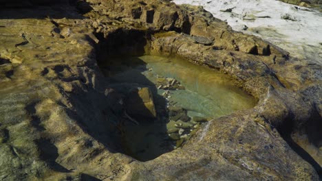 Small-rock-pool-during-golden-hour-cut-out-by-years-of-erosion,-ancient-rock