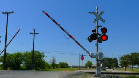 Bahnübergang-Mit-Blinkenden-Roten-Lichtern-Und-Herunterfahrenden-Schranken-Und-Vorbeifahrendem-Zug