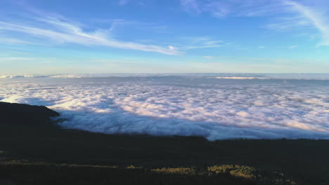 Blick-Auf-Eine-Dichte-Wolkenumkehr-Unterhalb-Des-Hangs-Des-Pico-De-Teide-Auf-Der-Kanarischen-Insel,-Beleuchtet-Von-Der-Abendsonne-Und-Einem-Blauen-Himmel-Darüber