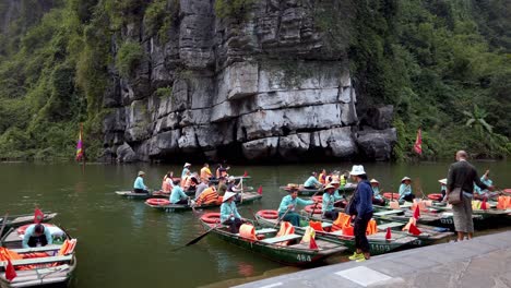 Paddleboats-arriving-at-a-loading-dock-on-the-Day-River-overlooking-limestone-karst-mountain-formation,-Handheld-shot