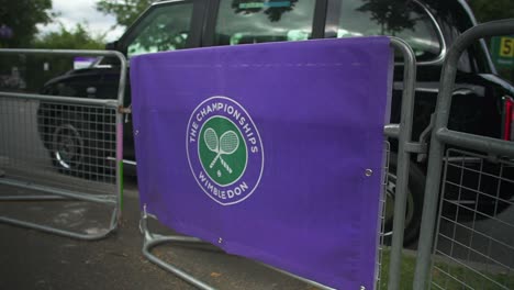Wimbledon-2019:-view-of-the-street-fence-with-Wimbledon-logo-on-it,-with-a-black-cab-in-the-background