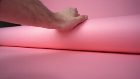 Hand-unrolling-pink-background-paper-for-a-photo-and-video-shoot-and-rolling-over-camera---still-shot