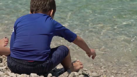 Caucasian-boy-playing-with-pebbles-at-the-beach-of-Fragolimano,-Corinth,-Greece