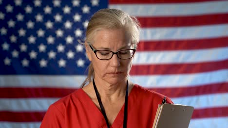 Portrait-of-nurse-set-against-an-out-of-focus-US-flag-showing-disappointment-and-sadness