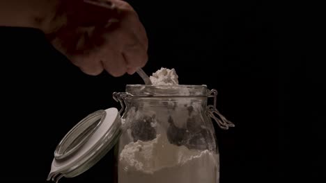 Taking-flour-from-a-jar-with-a-tablespoon-close-up-on-a-black-backdrop