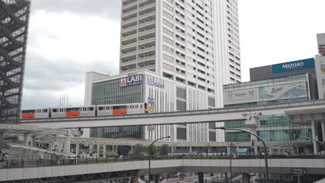 Un-Tren-Monorraíl-Que-Pasa-Por-Encima-De-La-Pasarela-Con-Edificios-De-Gran-Altura-En-El-Fondo-En-Tokio,-Japón
