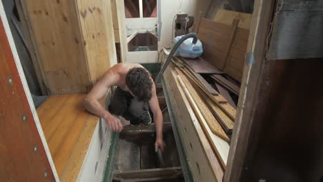 Young-man-hoovering-bilge-of-wooden-boat-interior