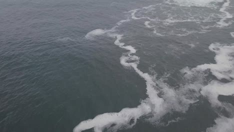 Slow-aerial-tilt-from-seafoam-to-horizon-on-misty,-grey-Indian-Ocean