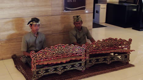 Dos-Hombres-Tocando-Música-Oriental-Usando-Un-Instrumento-Musical-Tradicional-Para-Recibir-A-Los-Huéspedes-Dentro-Del-Vestíbulo-De-Un-Hotel-En-Bali,-Indonesia