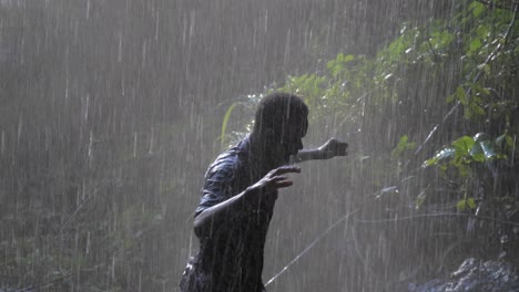 Close-up-slow-motion-shot-of-a-happy-African-man-dancing-under-the-spray-of-a-tropical-waterfall-while-getting-wet