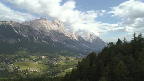 Amazing-Aerial-Passing-Trees-Revealing-the-Italian-Dolomites-with-Small-Town-in-the-Foreground