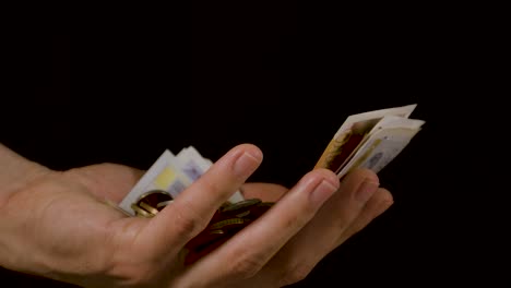 Coins-and-cash-money-falling-into-a-hand-against-a-black-background-in-slow-motion