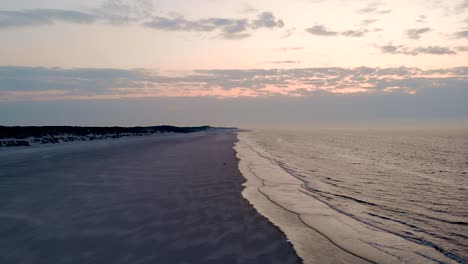 Drone-Over-Calm-Waves-At-Beach-With-Pink-Hue-From-Sunset-Sky-In-Langeoog-Island,-Germany