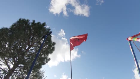 Proud-Albanian-Flag-waving-in-the-wind-against-the-blue-sky-on-top-of-flag-pole---Wide-Low-angle-shot