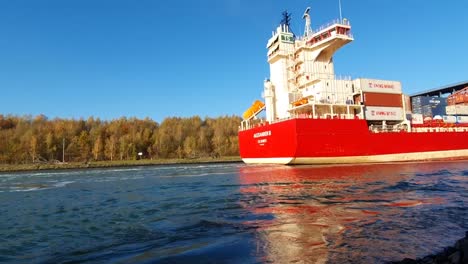 Rotes-Containerschiff,-Das-Fracht-Auf-Einem-Klaren-Fluss-Transportiert,-Sonniger-Himmel