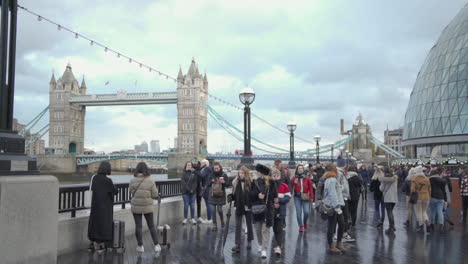 London-England-Skyline-and-People-Walking-by-Thames-River-and-City-Hall-Building-With-Tower-Bridge-in-Background,-Slow-Motion