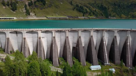 Dam-Wall-of-Lake-Fedaia-in-the-Dolomite-mountains-of-northern-Italy-with-people-and-cars-moving-on-the-top,-Aerial-Drone-left-pan-reveal-shot