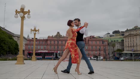 Two-skilled-tango-dancers-doing-a-difficult-routine-in-a-square-of-Buenos-Aires-with-Casa-Rosada-in-background