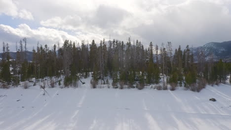Die-Luftaufnahme-Bewegt-Sich-Vorwärts-Und-Nach-Oben-Und-Zeigt-Einen-Eisigen,-Zugefrorenen-See,-Umgeben-Von-Schnee-Und-Grünen-Kiefern,-Mit-Großen-Schneebedeckten-Skiortbergen-Im-Hintergrund-In-Der-Nähe-Von-Silverthorne-Und-Frisco,-Colorado
