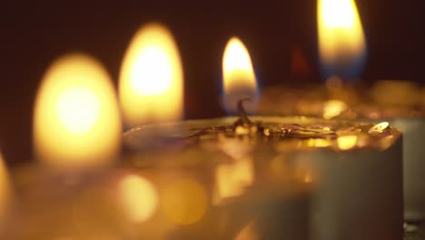 Focus-pull-from-far-to-near-along-a-line-of-candles-with-their-golden-flames-flickering-in-the-darkness---static-macro