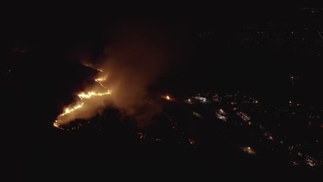 Brush-fire-on-mountainside-with-lights-of-town-in-dark-background