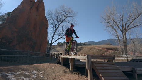 Man-jumps-off-of-wooded-structure-on-a-mountain-bike-in-Colorado-Springs,-Colorado