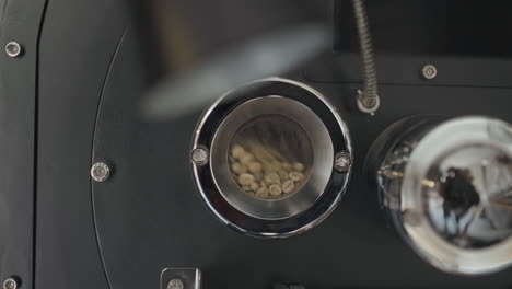 Kleine-Glasfensteröffnung-Einer-Kaffeeröstmaschine-Mit-Großem-Metallofen,-Die-Sich-Im-Zeitlupentempo-Heftig-Bewegt