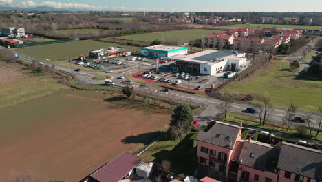 Aerial-View-Of-Traffic-Driving-Along-Commercial-Area-With-Food-Market,-Fast-Food-And-Shops-Near-Residential-Area-In-Arcore,-Northern-Italy