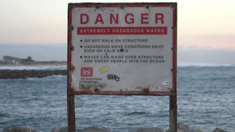 DANGER-sign-warns-people-of-the-extreme-hazards-of-climbing-on-jetties,-and-getting-too-close-to-the-turbulent-waves-that-have-caused-many-drownings-and-injuries-throughout-the-Bay-Area