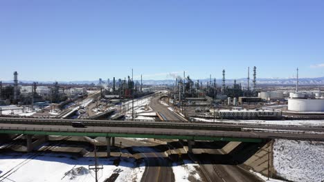 The-aerial-view-moves-up-to-show-a-Refinery-and-highway-with-Downtown-Denver-and-mountains-in-the-background