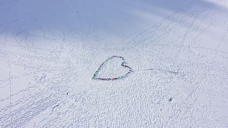 Beautiful-shot-of-heart-shaped-artwork-in-the-snow---Frozen-colored-water-laid-down-on-frozen-lake---Sunny-day-aerial