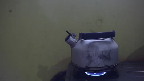 Metal-colored-kettle-with-boiling-water-on-a-stove-in-poor-kitchen