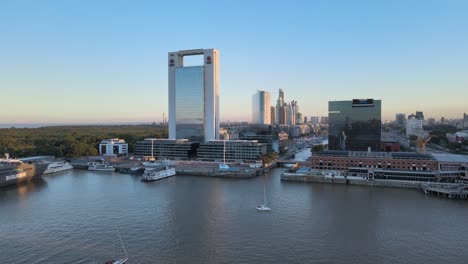 Aerial-dolly-out-of-boats-sailing-in-Puerto-Madero-docks-with-skyscrapers-in-background-at-sunset,-Buenos-Aires