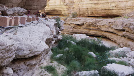 Hikers-walking-beside-the-pools-of-Wadi-Shab-canyon,-Oman,-wide-shot