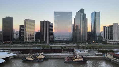 Aerial-dolly-out-of-boats-in-Puerto-Madero-docks-with-high-rise-buildings-in-background-at-sunset,-Buenos-Aires