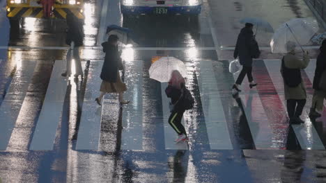 Gente-Con-Paraguas-Corriendo-Para-Cruzar-La-Calle-En-Una-Noche-Lluviosa-En-Tokio,-Japón