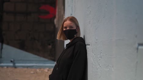 Young-Lonely-Female-With-Facemask-Behind-Wall-in-Urban-Exterior,-Slow-Motion