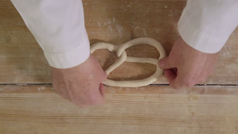 Handmade-German-pretzel-formed-by-baker-on-wooden-table-in-traditional-bakery