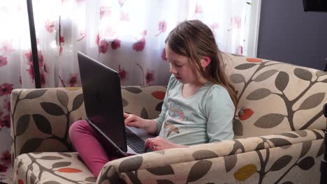 Distance-Learning---Cheerful-Little-Girl-Using-Laptop-Computer-Studying-Through-Online-E-Learning-System---wide-shot