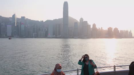 Frauen-Machen-Fotos-Und-Selfies-Entlang-Der-Uferpromenade-Von-Victoria-Harbour-Und-Genießen-Dabei-Den-Blick-Auf-Die-Skyline-Der-Insel-Hongkong,-Während-Der-Sonnenuntergang-Untergeht